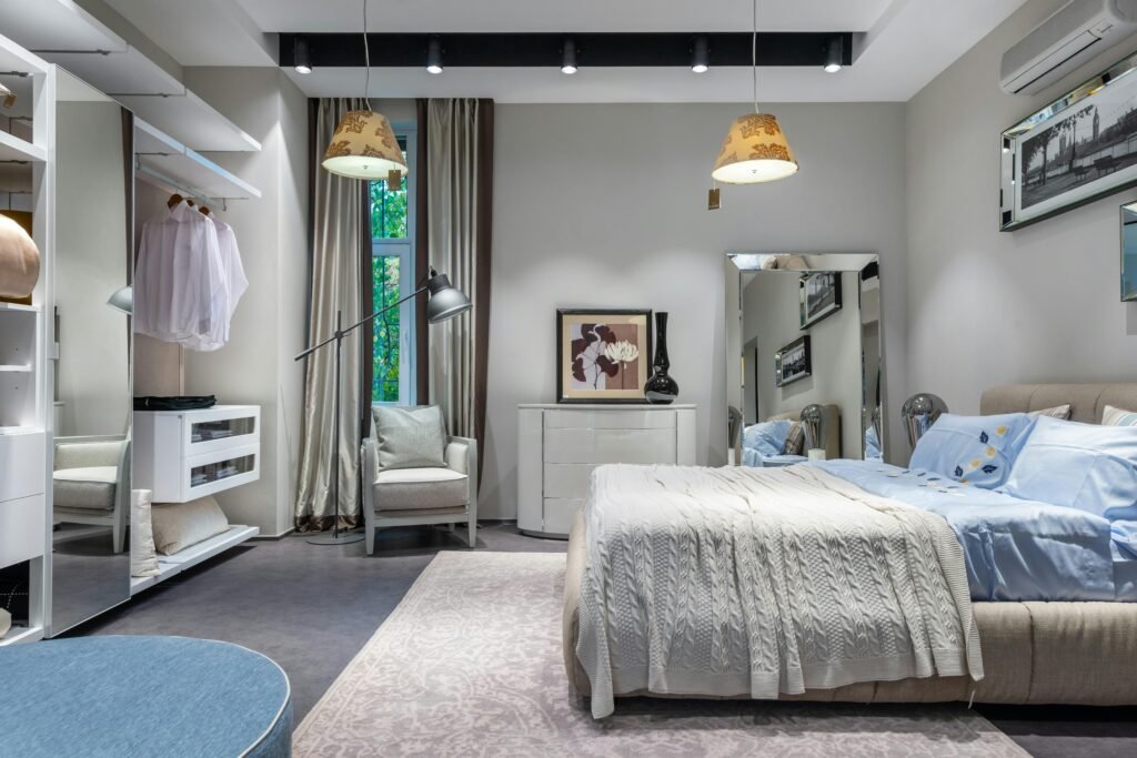 Comfortable bedroom with knitted coverlet and cushions built in spacious wardrobe armchair chest and mirror and hanging lamps