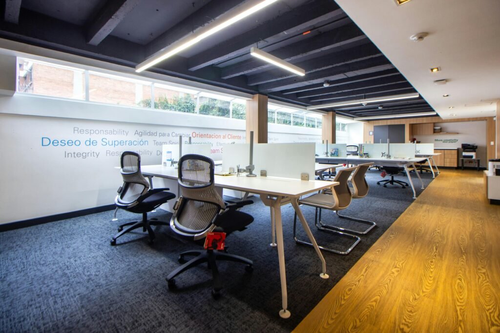 A well-lit, modern office space featuring ergonomic chairs, tables, and glass dividers.